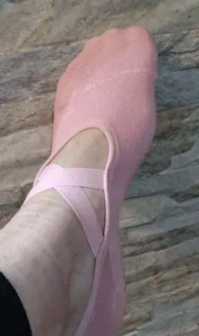 Close-up van een voet in een roze balletsok: de gekruiste bandjes lopen over de open wreef, de tenen blijven bedekt.