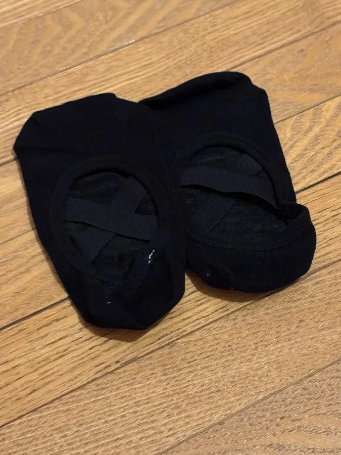 Een zwart paar balletsokken plat op een eikenhouten vloer, met de gekruiste bandjes over de open wreef.