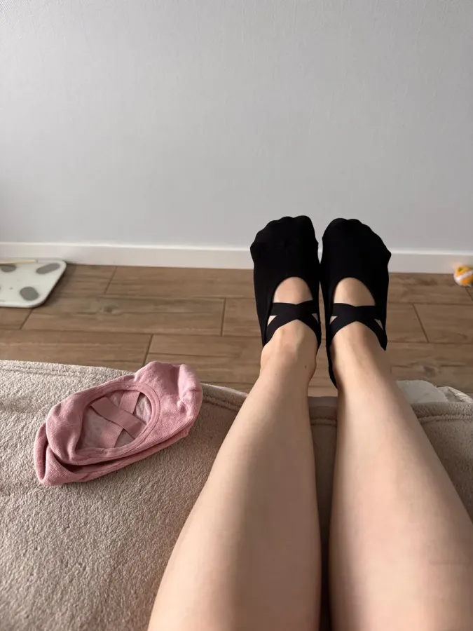 Twee voeten in zwarte balletsokken met gekruiste bandjes, benen gestrekt op een deken; ernaast ligt een roze balletsok.